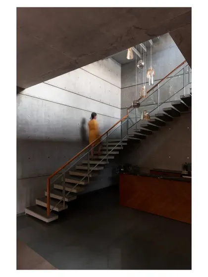 A figure ascends the staircase, providing a sense of scale and showing how light from a high skylight washes over the textured concrete walls.