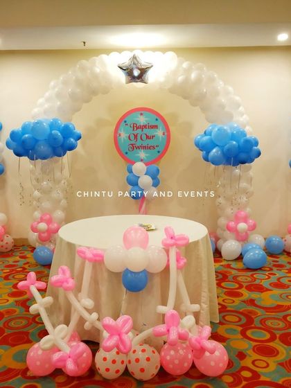 A baptism ceremony decoration for twins. The setup uses pink and blue balloon arrangements with a central table for the ceremony.