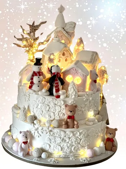 A magical winter wonderland cake. This glowing two-tiered creation features a whole snowy village scene with adorable snowmen and teddy bears.