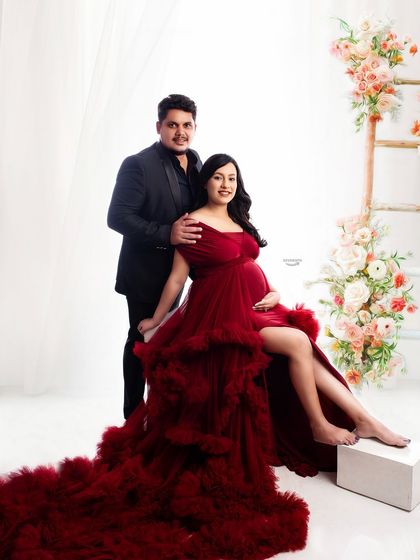 An elegant couple portrait with a floral ladder prop. The client's dramatic red gown and her partner's classic suit create a sophisticated and romantic image.