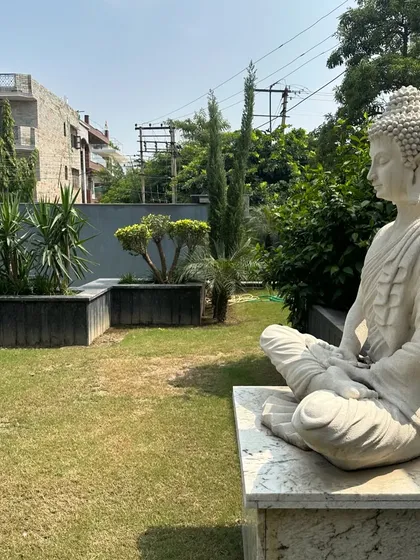 A side profile of the Buddha statue, looking out over the peaceful garden. The simplicity of the lawn and the surrounding trees enhances the meditative quality of the space.