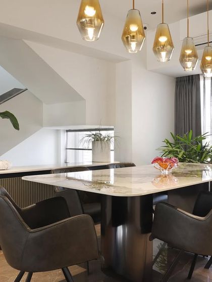 A dining area where culinary delights and warm ambiance intertwine. The marble-topped table, comfortable upholstered chairs, and amber glass pendant lights create a refined and welcoming space for meals.