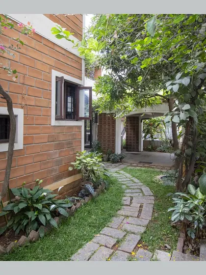 A stone-paved path winds through a side garden, leading towards the car porch.