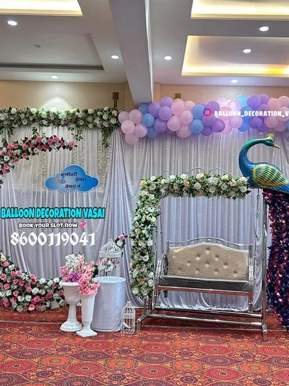 An elegant hall setup featuring a floral crescent moon arch and a stunning peacock next to the baby's jhula. The pastel purple and blue balloons add a soft and dreamy quality to the entire stage.