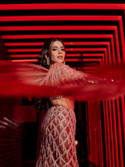 A dramatic shot of the bride, with the red light creating a powerful backdrop for her shimmering, contemporary lehenga.