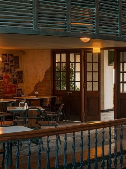 The view into a semi-private dining area, framed by the balcony above. The louvered panels and traditional wooden doors add to the old-world charm.