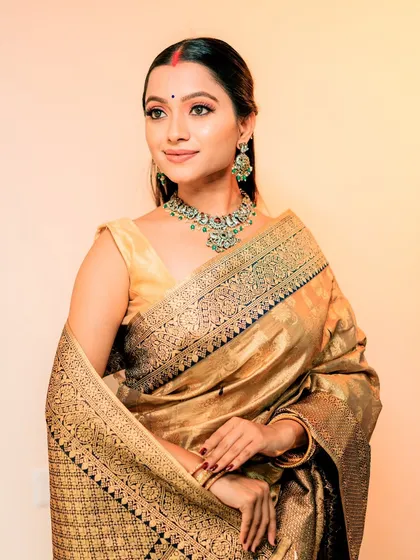 A close-up of the model's makeup, featuring a red bindi and jewellery with green accents.