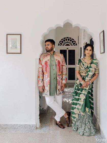 A stylish, editorial-style portrait of the couple posing in a white corridor, showcasing their high-fashion wedding attire.