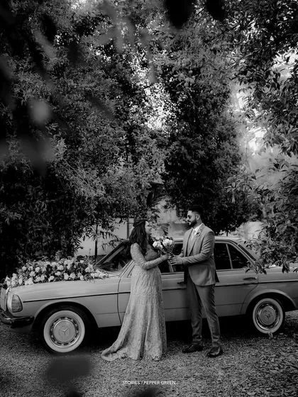 A timeless black and white photo of Ameera and Richard by their classic car. This editing style adds a touch of elegance and nostalgia to their story.