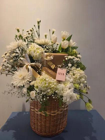 Another view of the all-white floral basket, showcasing the natural texture of the wicker and the soft glow of the satin ribbons. This is a perfect gift for birthdays or to offer congratulations.