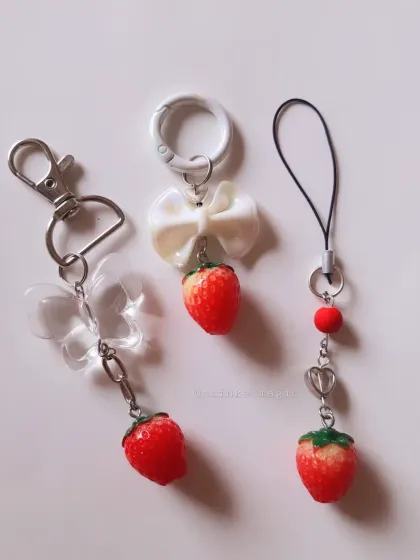 A trio of sweet strawberry charms. This image shows the different ways you can use them: as a bag charm with a butterfly, a keychain with a bow, or a phone charm with a heart.