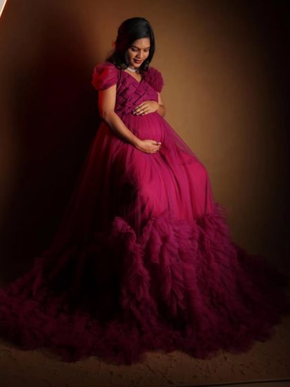 A classic seated portrait from a maternity session. This photo highlights the delicate floral shoulder detail and the rich color of the magenta ruffled gown, a popular rental for expecting mothers.