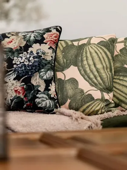A close-up shot of beautifully patterned cushions on a sofa, with a lit candle in the foreground. This image captures the cozy and intimate details that make a house feel like a home.