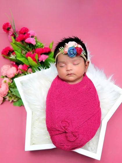 This little girl is swaddled in a vibrant pink wrap, resting in a star-shaped prop. The bright colors and floral accents make for a cheerful and eye-catching portrait.
