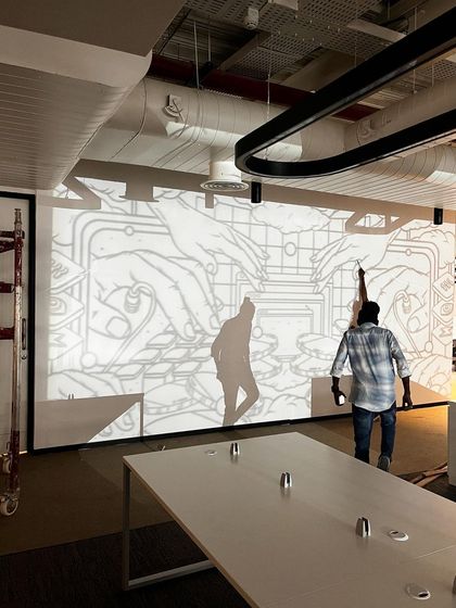 A process shot showing the initial projection of the line art onto the wall, the first step in translating the digital design to a physical mural.