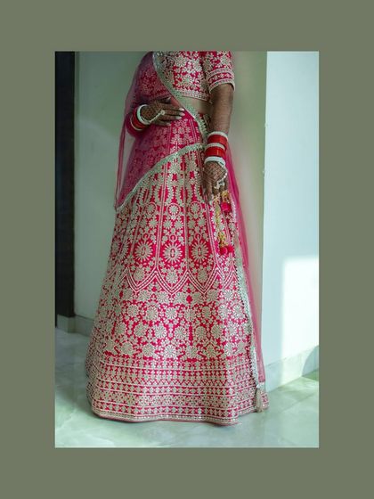 A full-length portrait of a bride in a stunning pink lehenga. The simple background makes her vibrant outfit and happy expression the center of attention.