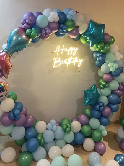 Dive into an under-the-sea adventure with this mermaid theme. A beautiful balloon ring in shades of purple, green, and blue, complete with a mermaid tail foil balloon and a neon sign, creates a magical photo corner.