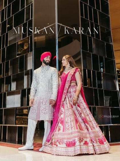 The couple stands hand-in-hand in a modern, reflective lobby, their traditional outfits creating a beautiful contrast with the contemporary architecture in Bangkok.