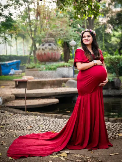 This mom-to-be looks absolutely radiant in a classic red maternity gown with a long train, standing in a beautiful garden setting.