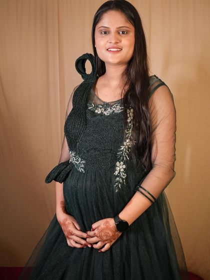 A simple and elegant solo portrait of an expecting mother in a dark green rental gown. The focus is entirely on her and her happy expression.