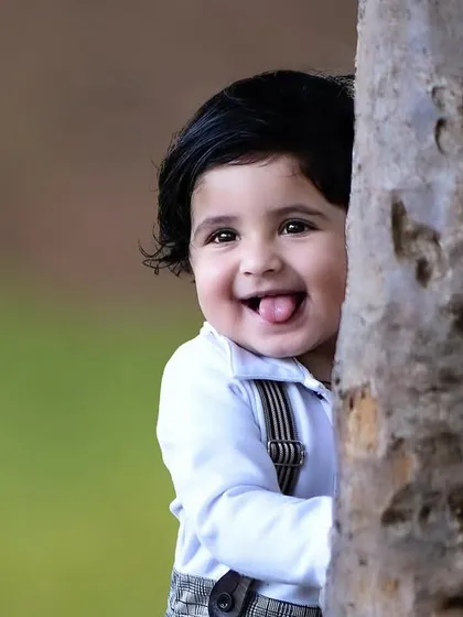 A playful close up of a one year old boy peeking from behind a tree and sticking his tongue out. It's these cheeky moments that make for unforgettable photos.