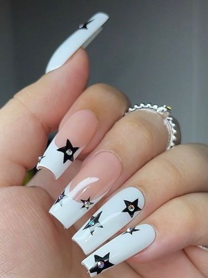 A statement-making French manicure with white tips on long coffin nails, decorated with black stars and sparkling rhinestones.