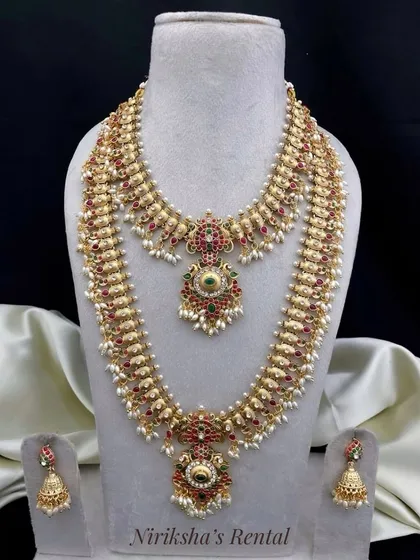 This bridal jewellery set features beautiful pearl detailing along with red and green stones, offering a grand look for a wedding day.