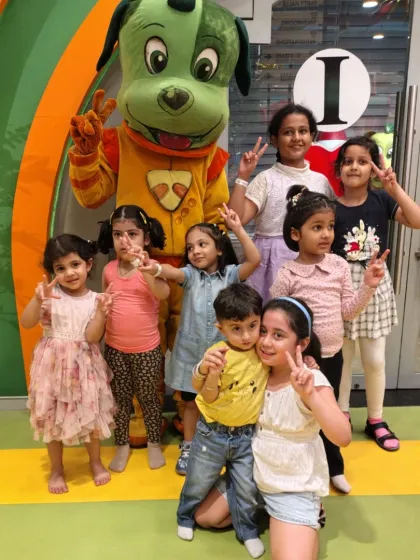 A group of children gathers around Tinga Dojo for a memorable photo, all flashing peace signs and big smiles.
