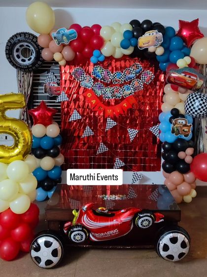 Ready, set, go! A Disney Cars themed party perfect for a little racer's 5th birthday. The setup includes a red foil curtain backdrop, checkered flag details, and a giant Lightning McQueen race car balloon.