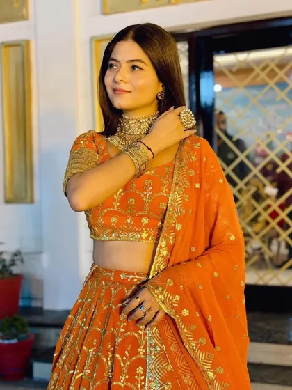 A close-up of the model in the orange lehenga, showcasing the choker necklace and statement ring.