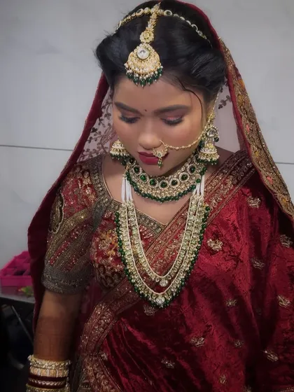 A close-up of a bride in a deep red lehenga. The focus is on the intricate jewelry and the perfectly blended makeup that complements the rich colors of her outfit.