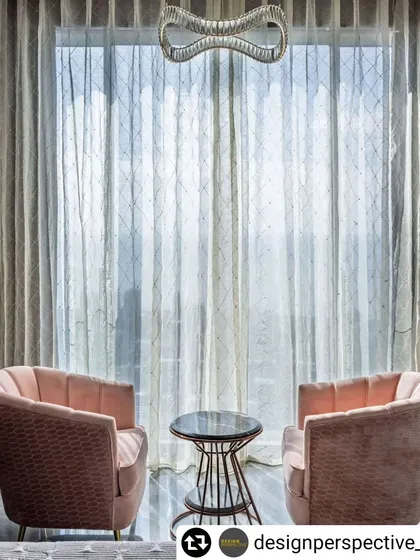 A quiet seating area in a luxury apartment, perfect for conversation. Two plush pink armchairs are set against a large window with sheer curtains, offering a beautiful view of the Mumbai skyline.