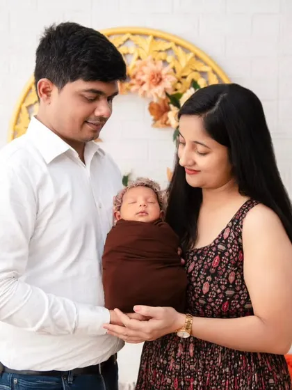 A newborn's first family portrait. We carefully pose the baby, swaddled in a warm brown wrap, in the loving hands of his parents for a timeless and classic shot.