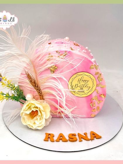 A unique and artistic dome-shaped cake for Rasna's birthday, decorated with feathers, gold leaf, and dried flowers for a boho-luxe vibe.