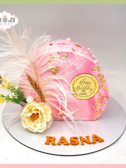 A unique and artistic dome-shaped cake for Rasna's birthday, decorated with feathers, gold leaf, and dried flowers for a boho-luxe vibe.