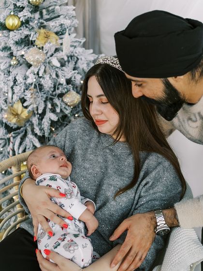 A family admiring their newborn baby by the Christmas tree. A baby's first Christmas is an incredibly special milestone to document.