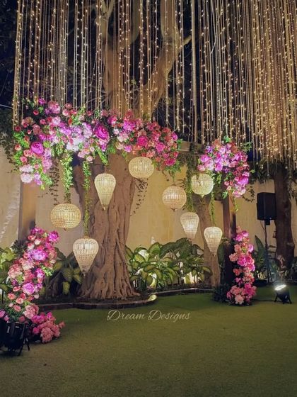 Pink hues and elegant chandeliers set the mood for this reception. I used clusters of pink flowers and hanging lanterns to decorate the space around a large tree, creating a natural yet glamorous focal point.