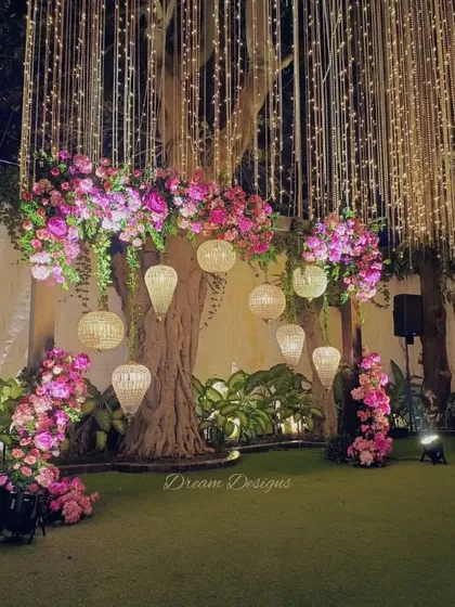 A beautiful backdrop for a reception, featuring a large banyan tree. I decorated its branches with clusters of pink flowers and elegant hanging lanterns to create a romantic and natural photo spot.