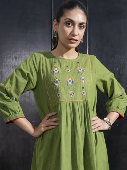 A close-up of the Paheli green dress, showing the intricate embroidery on the yoke. The geometric patterns and vibrant colors are a hallmark of this collection.
