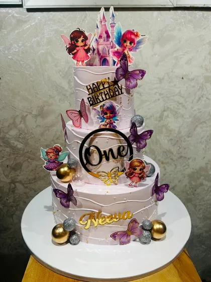 A whimsical three-tier fairy-themed cake for a first birthday, decorated with fluttering butterflies and sparkling gold and silver balls.