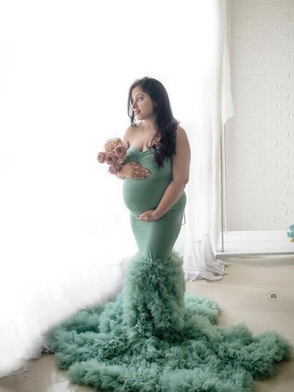 A classic solo maternity pose against a high-key white background, with the light beautifully shaping the expecting mother in her mint green gown.
