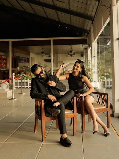 A cool and stylish candid shot of the couple sharing a playful moment indoors. Their all-black outfits and relaxed poses create a modern and chic vibe.