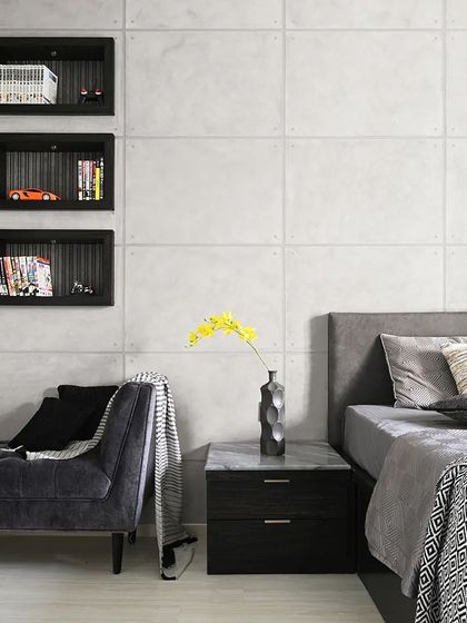 This bedroom demonstrates a minimalist, monotone approach. The wall behind the bed features a subtle concrete texture, while recessed black niches act as modern, integrated shelves for books and decor, maintaining a clean and uncluttered look.