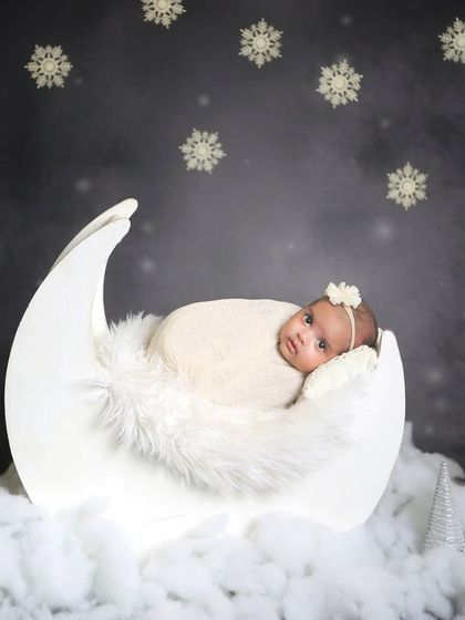 A winter wonderland theme with a baby in a moon prop, surrounded by fluffy "snow" and snowflake details. A magical setup for a winter baby.