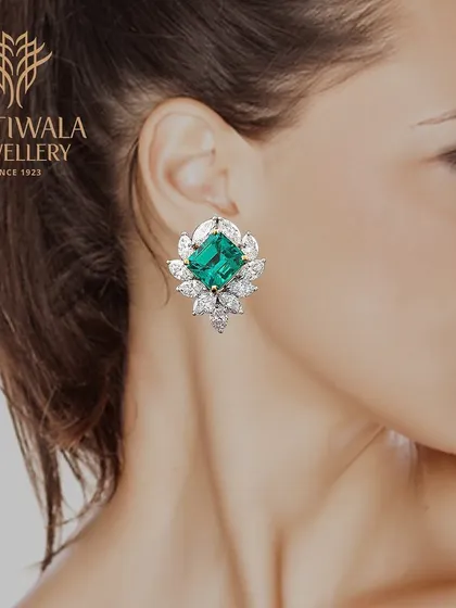 A model wears a pair of magnificent stud earrings with a central emerald surrounded by marquise-cut diamonds, perfect for a glamorous bridal look.