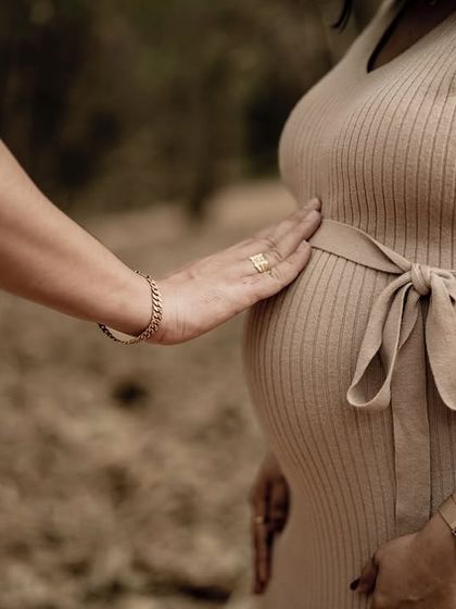 A gentle and loving close-up. The partner's hand rests tenderly on the baby bump, a simple gesture that speaks volumes about connection and support.