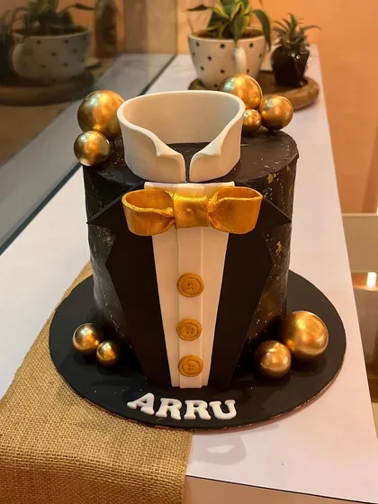 The perfect cake for a gentleman. This tuxedo cake features a sharp black finish with a geometric texture, a fondant collar, a gold bow tie, and elegant gold sphere accents for a sophisticated celebration.