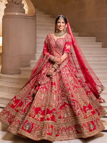 A magnificent full-length portrait showcasing a bride in a stunning red lehenga. The makeup is designed to be grand yet elegant, perfect for a palace wedding.