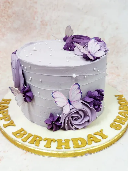 This elegant Purple Cake With Butterflies features delicate lavender frosting, piped pearls, and a cascade of purple sugar flowers and butterflies.
