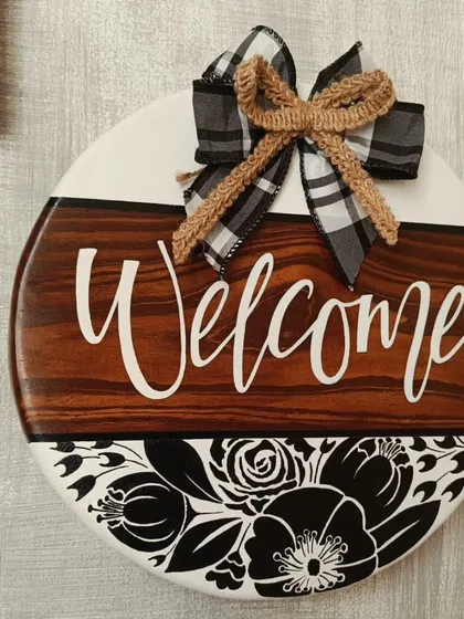 A classic "Welcome" sign to greet your guests. This piece combines a rich wood finish with bold floral graphics and a charming checkered bow, making any doorway feel more inviting.